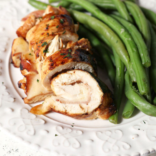 Close up of sliced chicken cordon bleu on a white plate next to steamed green beans