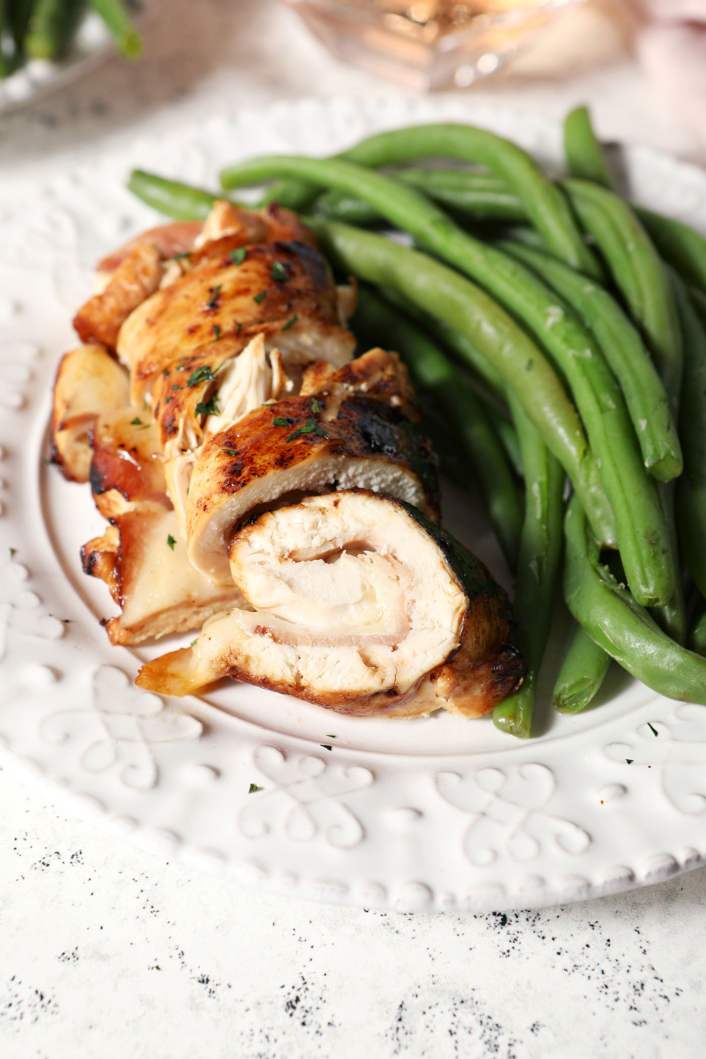Close up of sliced chicken cordon bleu on a white plate next to steamed green beans
