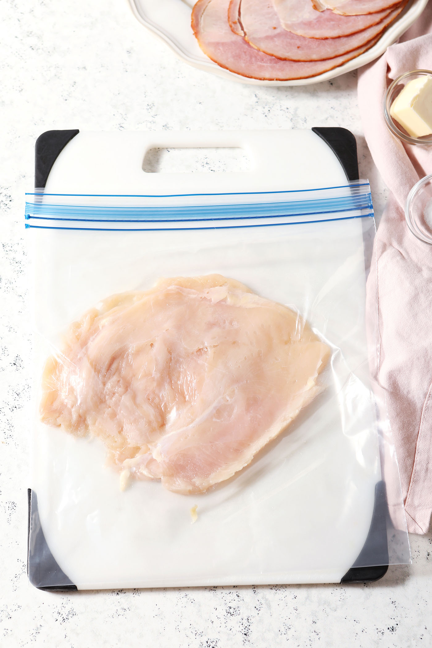 A flattened chicken breast in a gallon-sized plastic bag on a Cutting board
