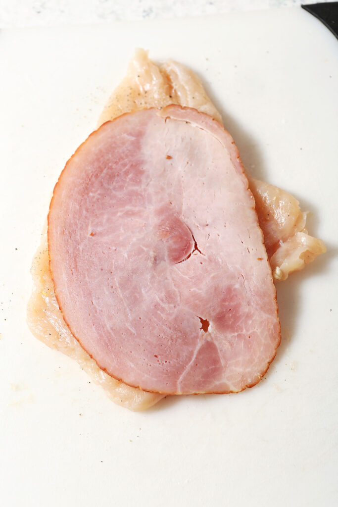 A slice of ham on top of a tenderized chicken breast