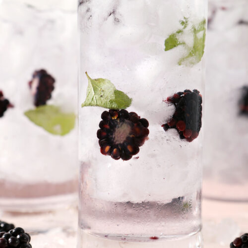 Close up of iced spa water with halved blackberries and mint leaves on a pink plate