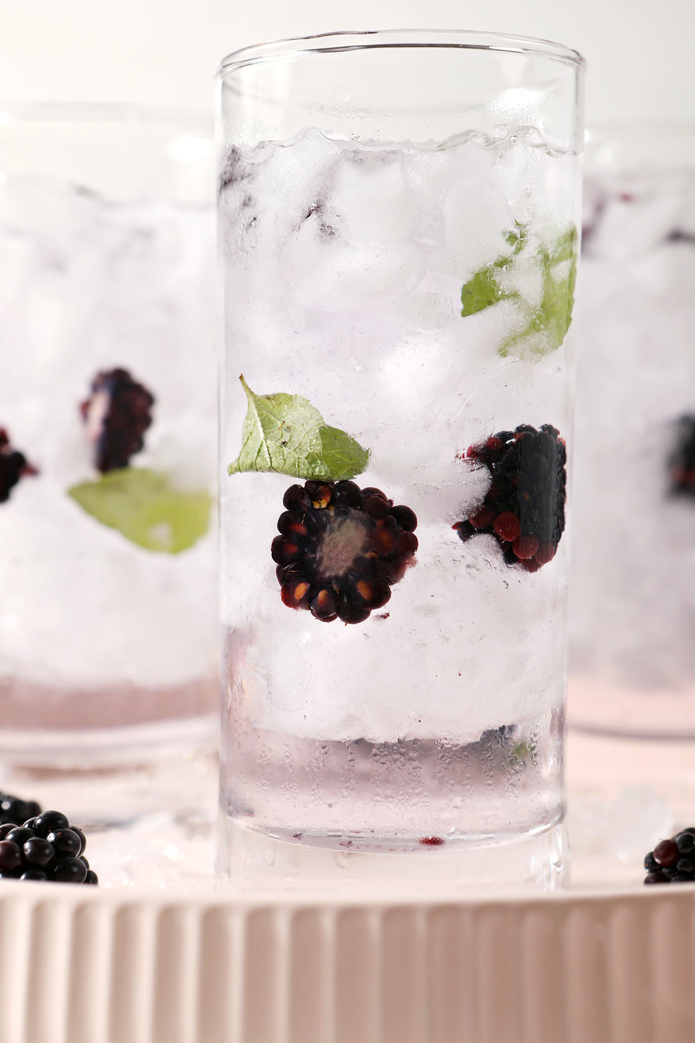 Close up of iced spa water with halved blackberries and mint leaves on a pink plate