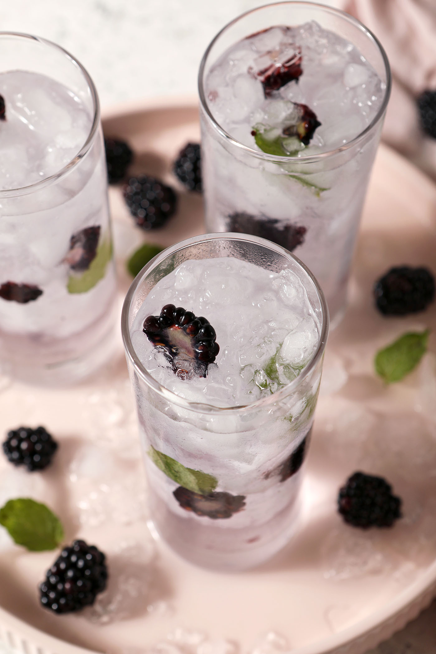 Overhead of three glasses of Blackberry Mint Spa Water on a pink plate decorated with berries and fresh mint leaves