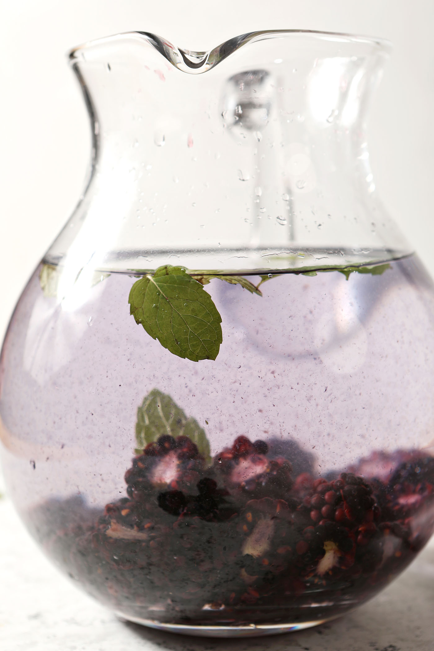A mint leaf floats on top of spa water filled with blackberries in a pitcher