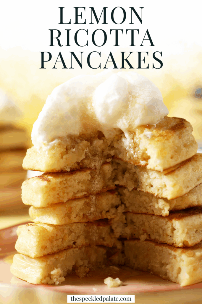 A cut into stack of pancakes topped with whipped cream and maple syrup on a pink plate on a yellow surface with the text lemon ricotta pancakes