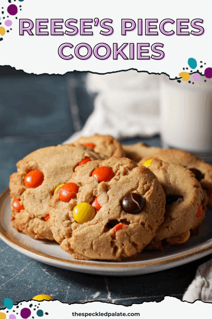 A plate of peanut butter cookies topped with Reese’s pieces sits on a teal tiled surface in front of a glass of milk with the text reese's pieces cookies