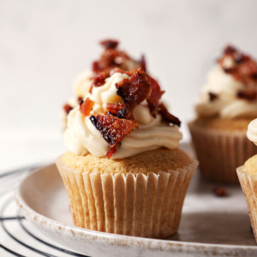 Close up of decorated Bourbon Maple Bacon Cupcakes on a grey plate on top of a wire cooling rack