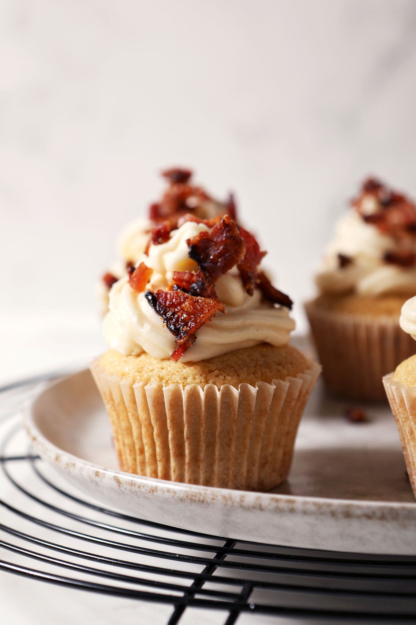 Close up of decorated Bourbon Maple Bacon Cupcakes on a grey plate on top of a wire cooling rack