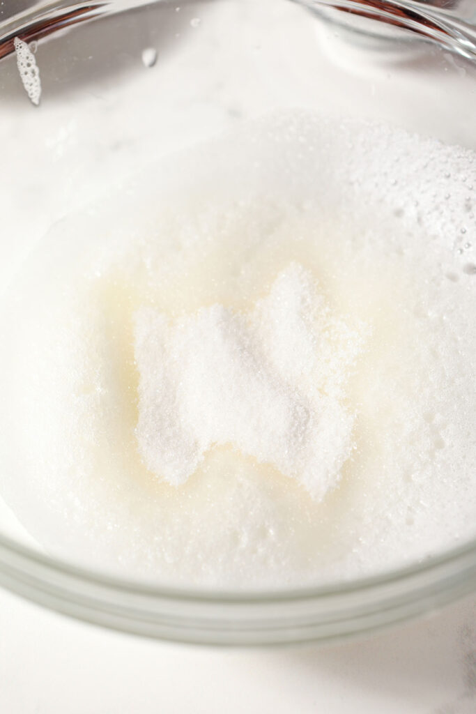 Sugar on top of whipped egg whites in a bowl