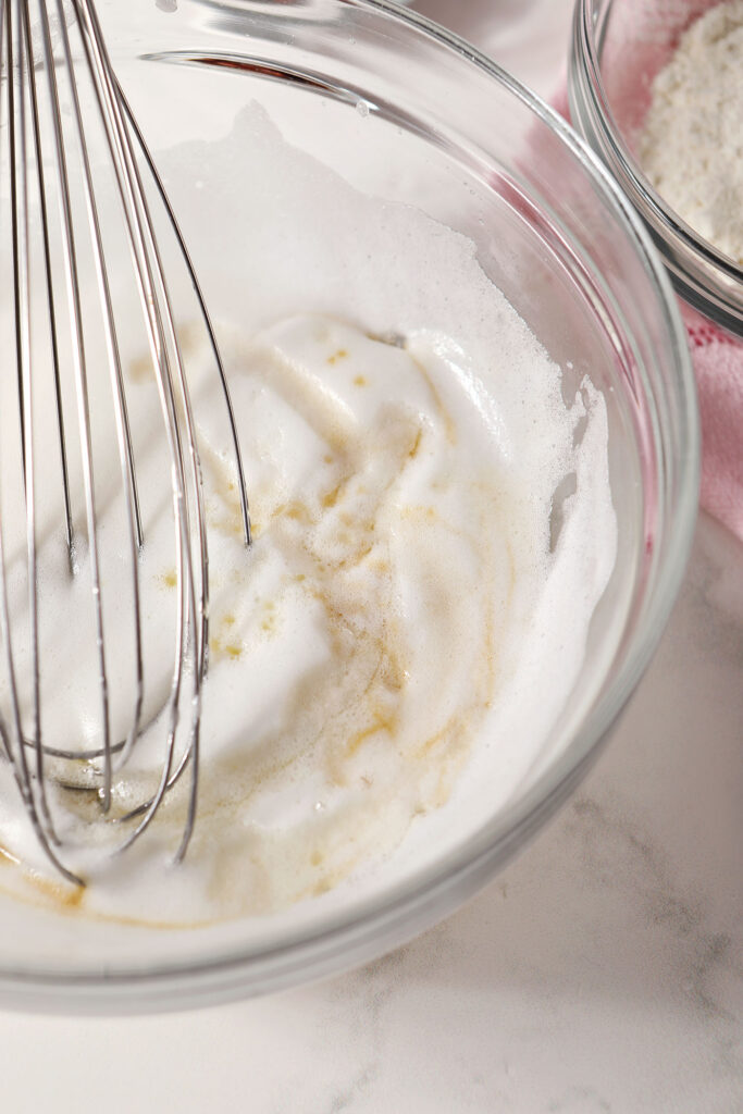 Close up of a whisk in a bowl with whipped egg whites and other wet ingredients for cupcakes
