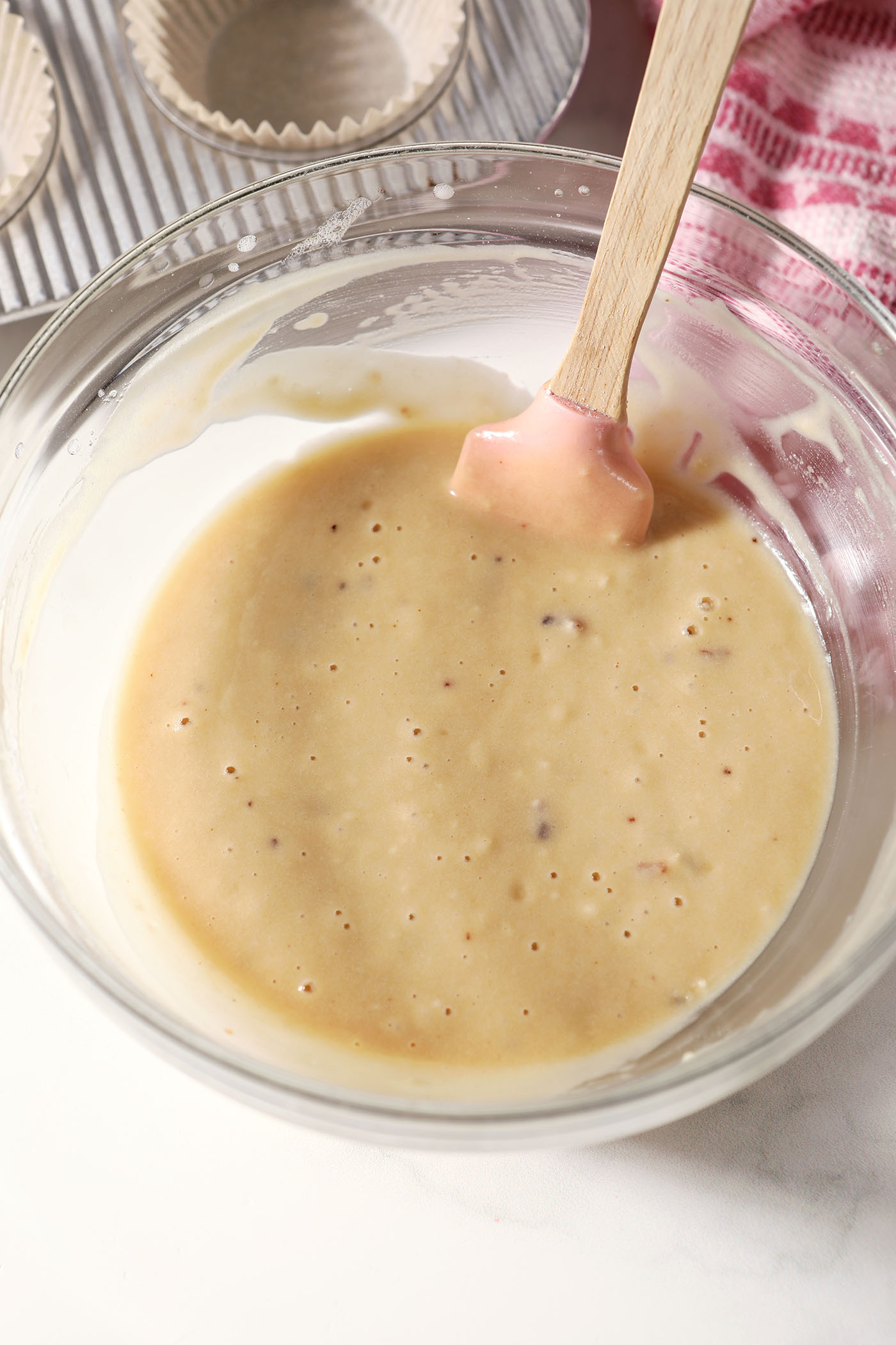Cupcake batter in a bowl next to a pink linen and a small cupcake pan