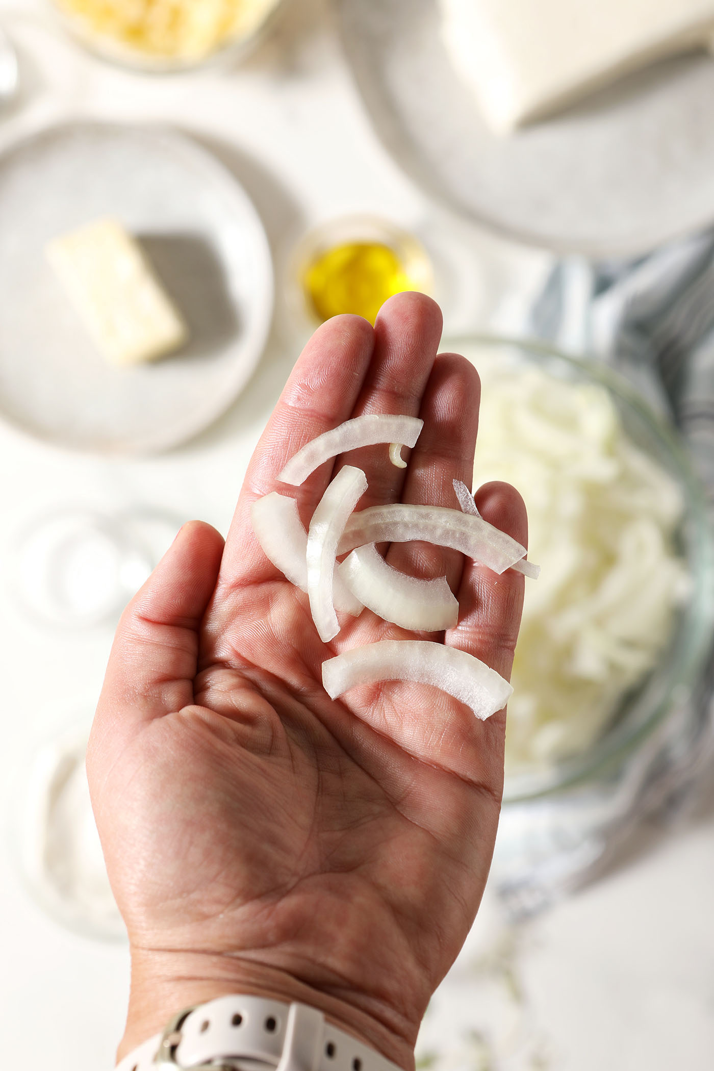 Sliced onions held in a hand above other ingredients
