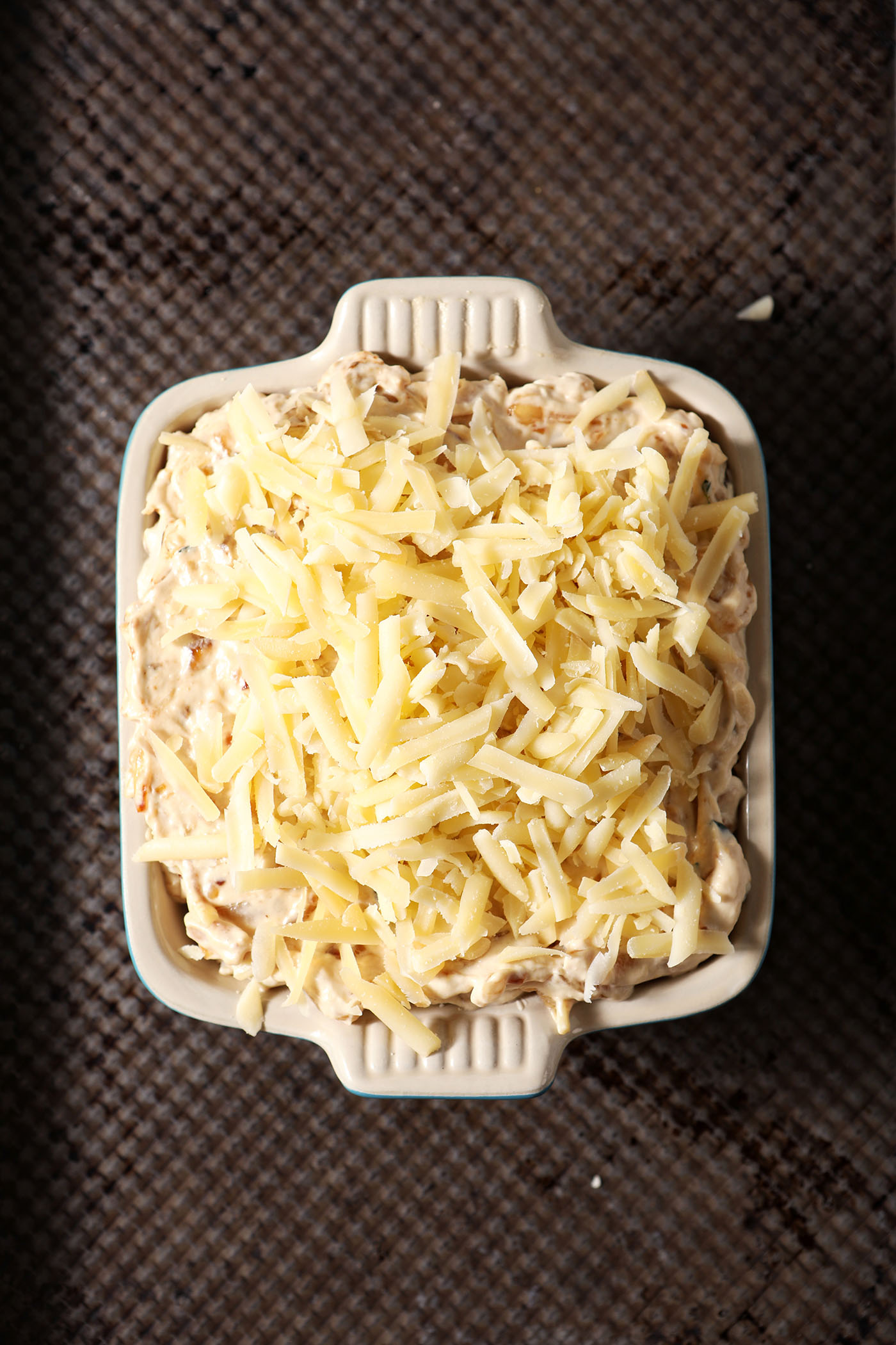 Overhead of shredded cheese on top of onion dip on a sheet pan before baking