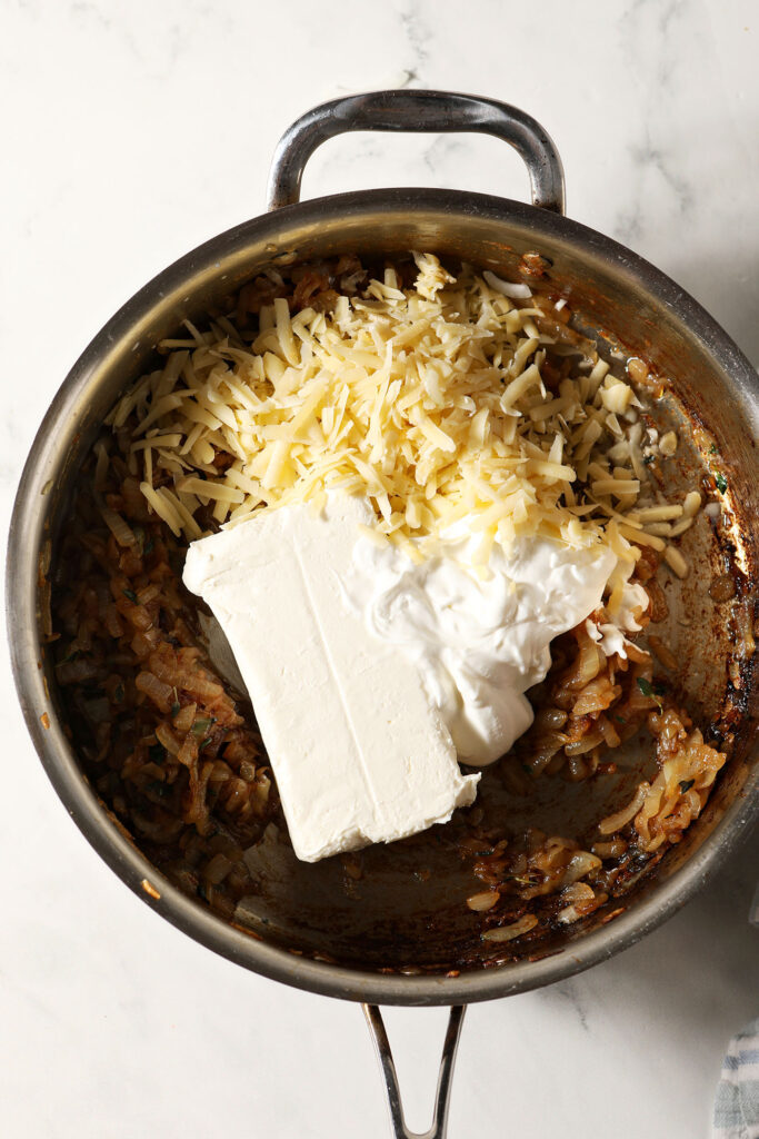 A block of cream cheese, sour cream and shredded gruyere sit on top of caramelized onions before stirring together