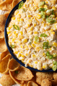 Close up of creamy corn dip from above, garnished with green onions and surrounded by corn chips