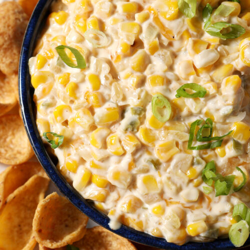 Close up of creamy corn dip from above, garnished with green onions and surrounded by corn chips