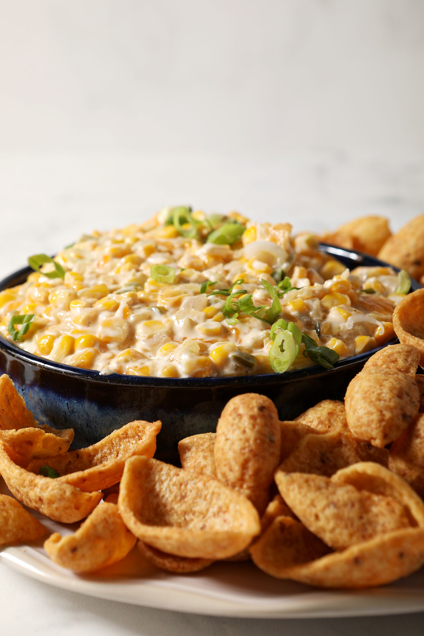 A bowl of hot corn dip from the side, surrounded by corn chips