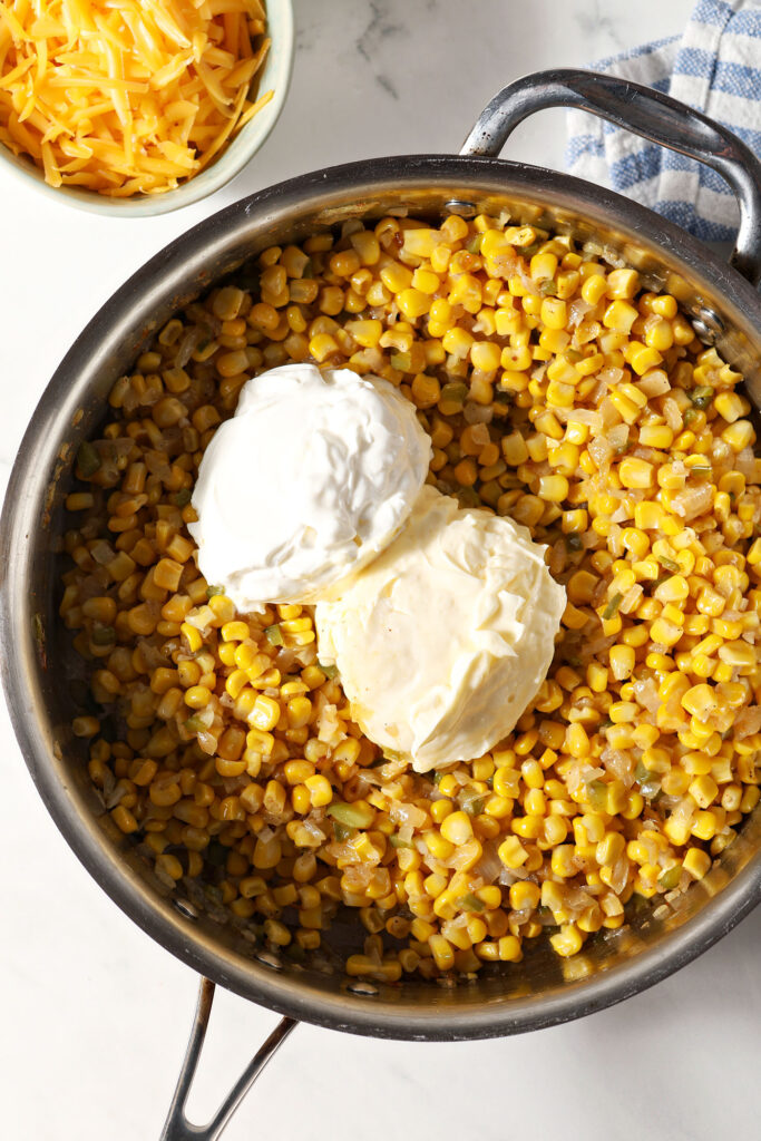 A scoop of mayonnaise and a scoop of sour cream on top of sautéed corn and veggies in a skillet