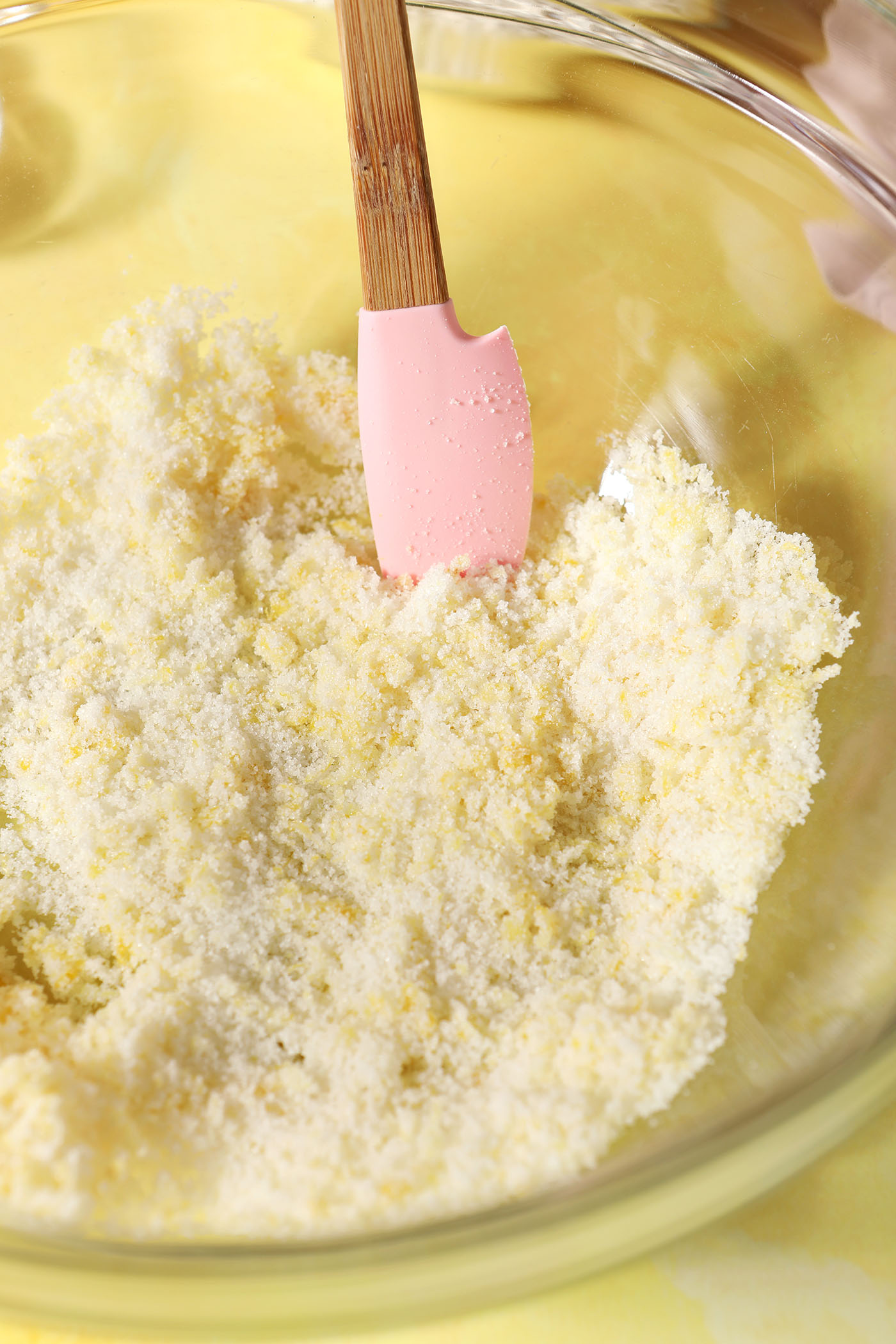 Lemon zest stirred into granulated sugar in a large bowl with a pink spatula