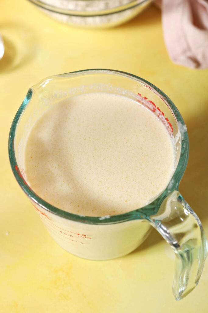Wet ingredients for pancakes in a liquid measuring cup on a yellow surface