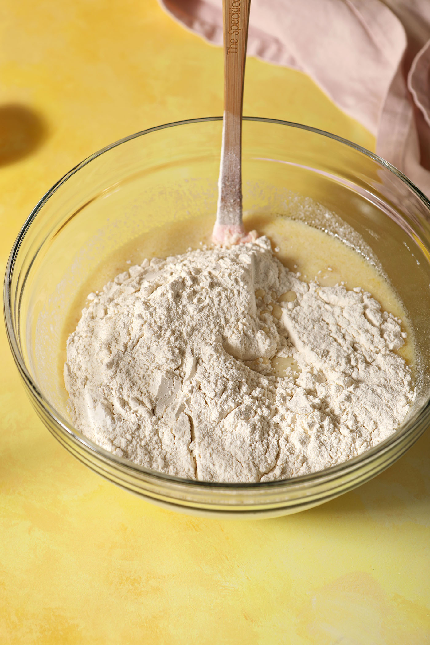 Dry ingredients on top of wet ingredients before mixing pancake batter together with a spatula on a yellow surface