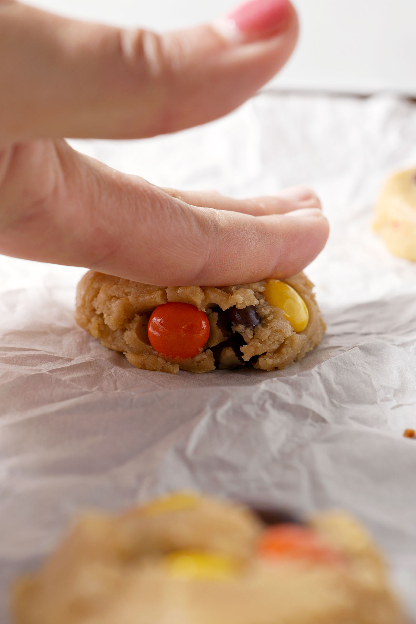 A hand presses a Reese’s Pieces Peanut Butter Cookie into shape on parchment