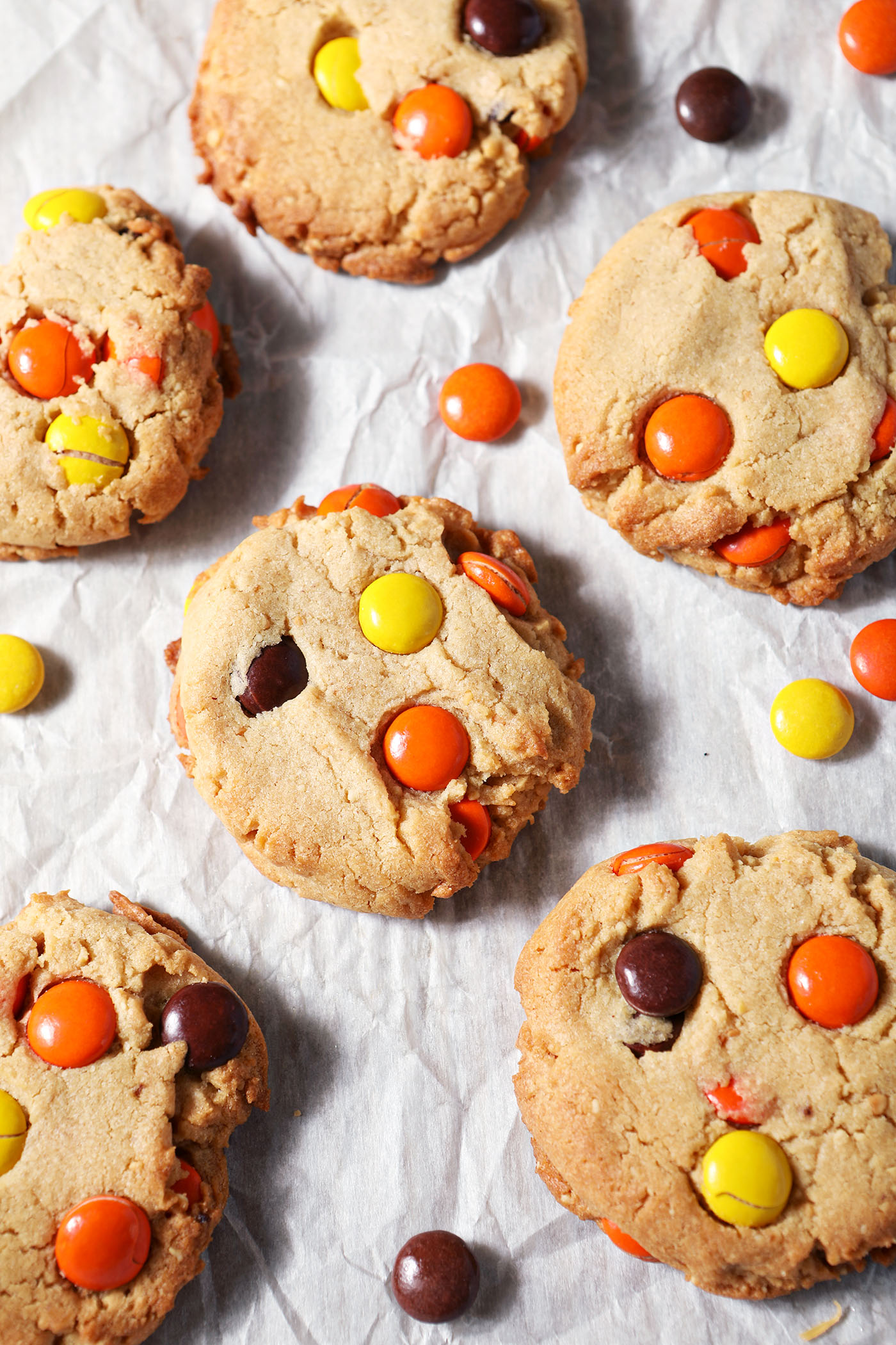 Baked Reese’s Pieces Peanut Butter Cookies surrounded by more Reese’s pieces on parchment paper