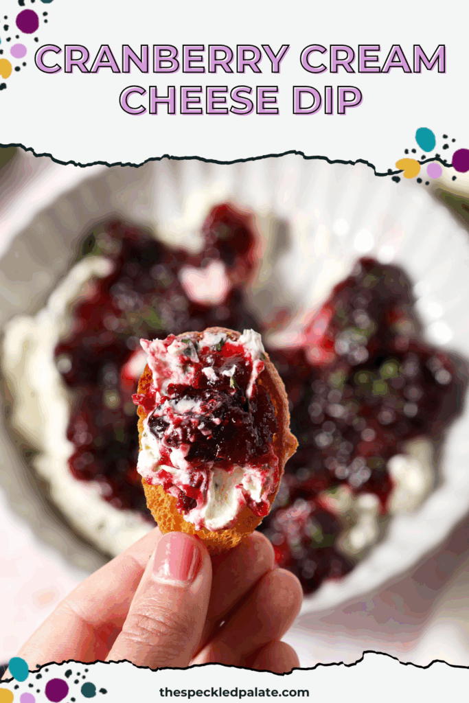 A hand holds a crostini holding cranberry cream cheese dip with jalapeño cream cheese over a platter with the dip with the text cranberry cream cheese dip