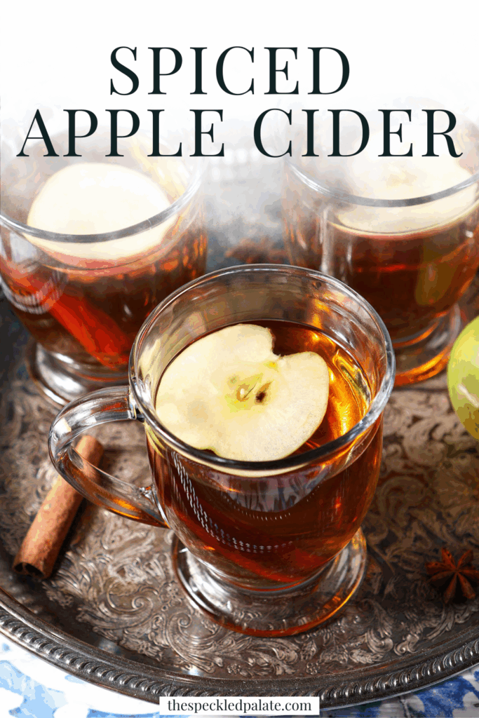 Close up of three glasses of hot cider topped with apple slices on a silver platter with the text spiced apple cider