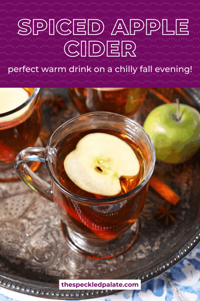 Close up of three glasses of hot cider topped with apple slices on a silver platter with the text spiced apple cider perfect warm drink for a fall evening