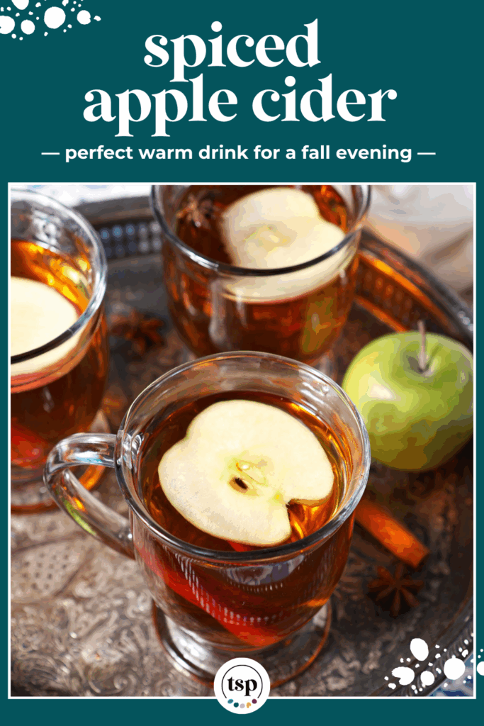 Close up of three glasses of hot cider topped with apple slices on a silver platter with the text spiced apple cider perfect warm drink for a fall evening