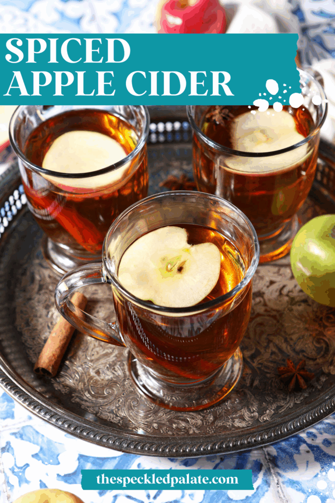 Close up of three glasses of hot cider topped with apple slices on a silver platter with the text spiced apple cider