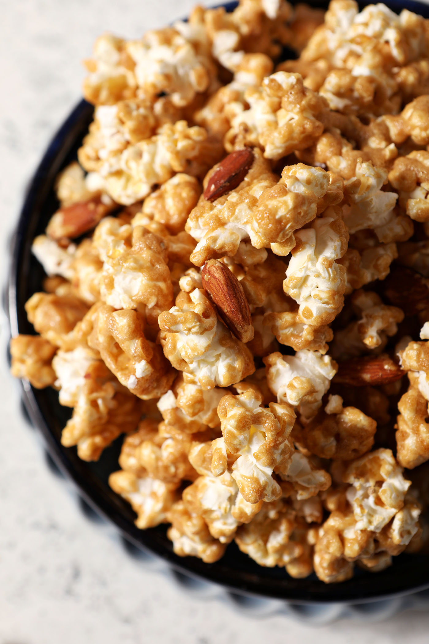 Overhead image of a bowl of caramel corn with almonds on a grey stone countertop