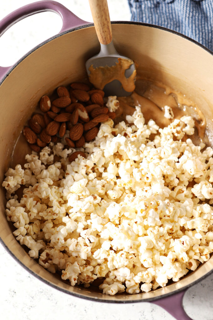 Popcorn and almonds on top of caramel in a dutch oven with a grey rubber spatula