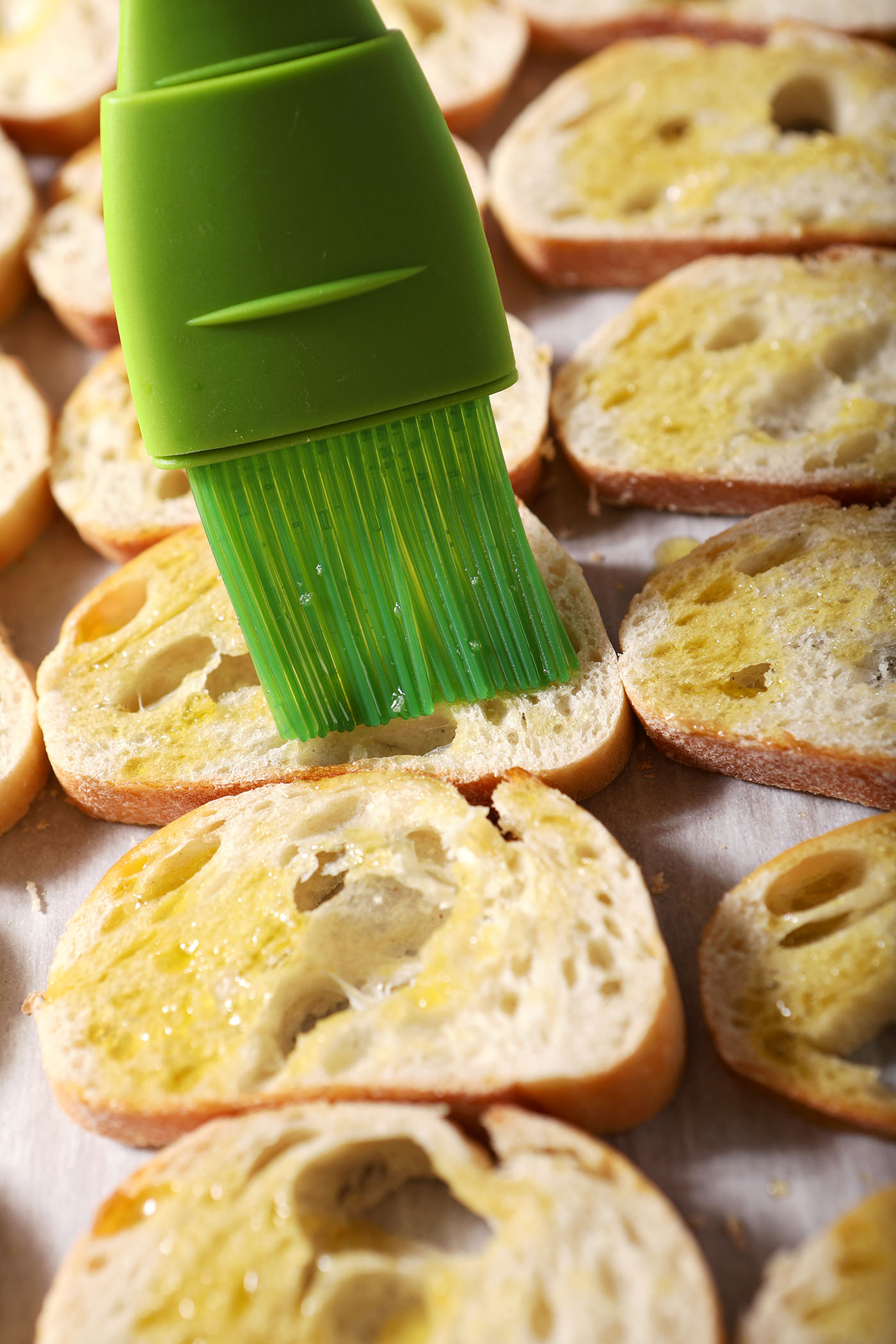 A green pastry brush brushes baguette rounds with oil