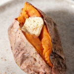 A roasted sweet potato with a pat of butter and sprinkled cinnamon on top on a grey plate