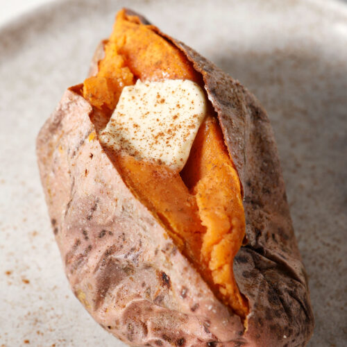 A roasted sweet potato with a pat of butter and sprinkled cinnamon on top on a grey plate