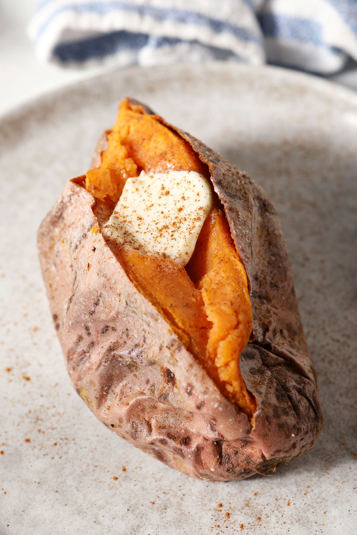 A roasted sweet potato with a pat of butter and sprinkled cinnamon on top on a grey plate
