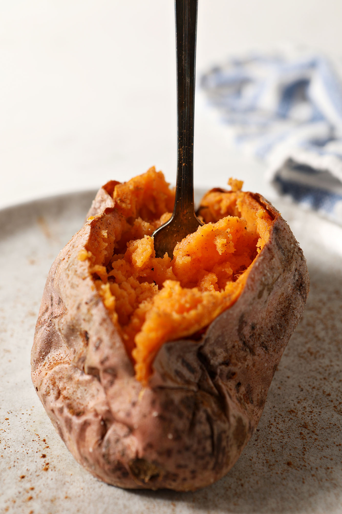 A fork spears the flesh of a halved roasted sweet potato on a grey plate