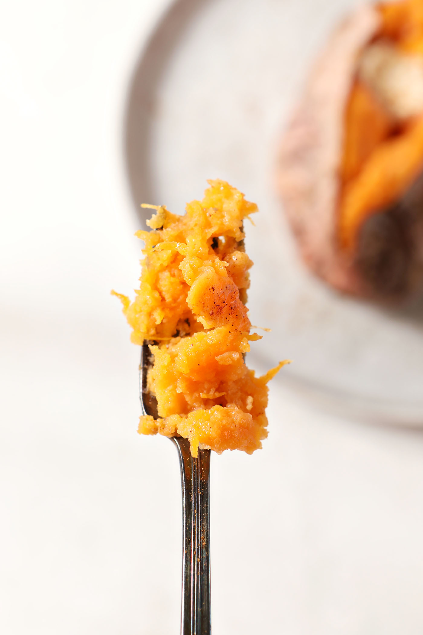 A fork holds a bite of roasted sweet potato above a plate with a sweet potato