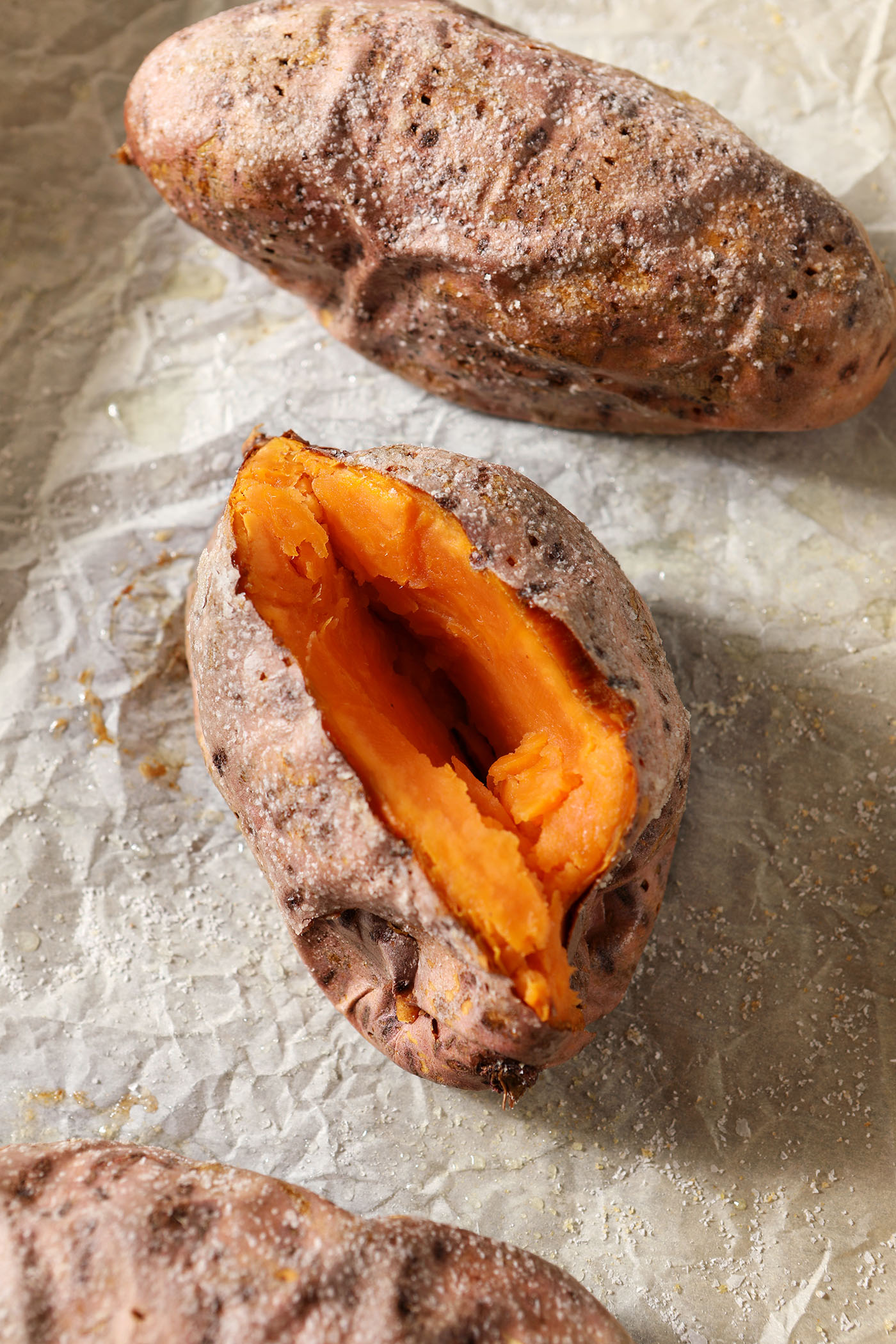 Three roasted sweet potatoes on a sheet pan, one cut in half