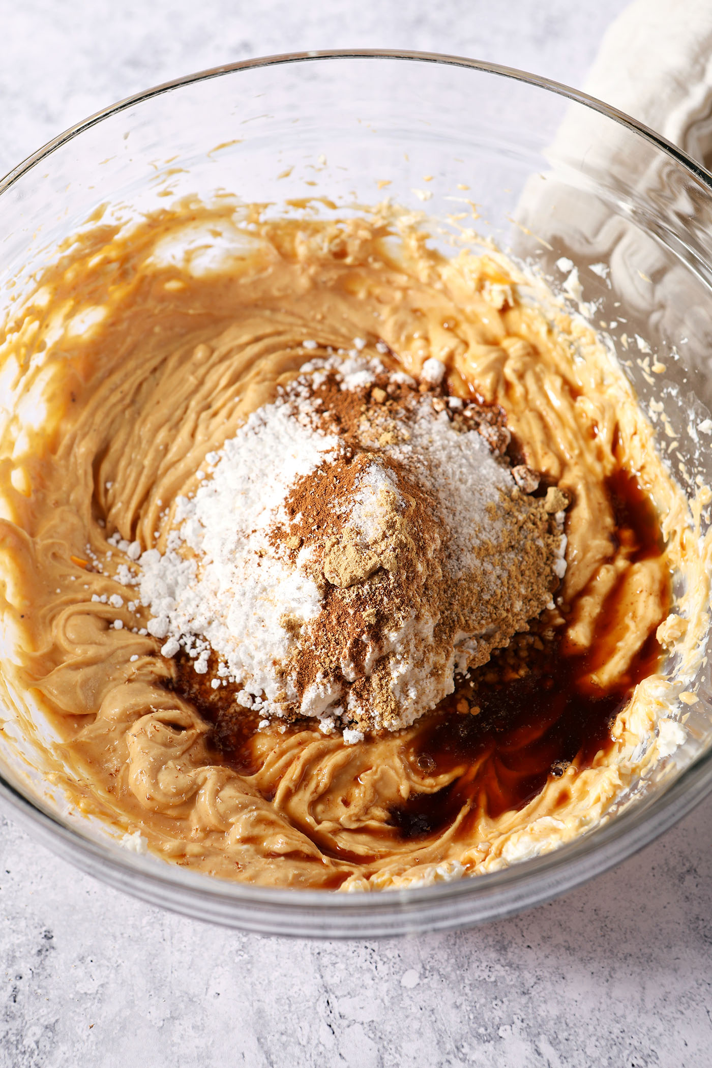 Powdered sugar, spices and vanilla extract sit on top of other pumpkin dip ingredients, before mixing