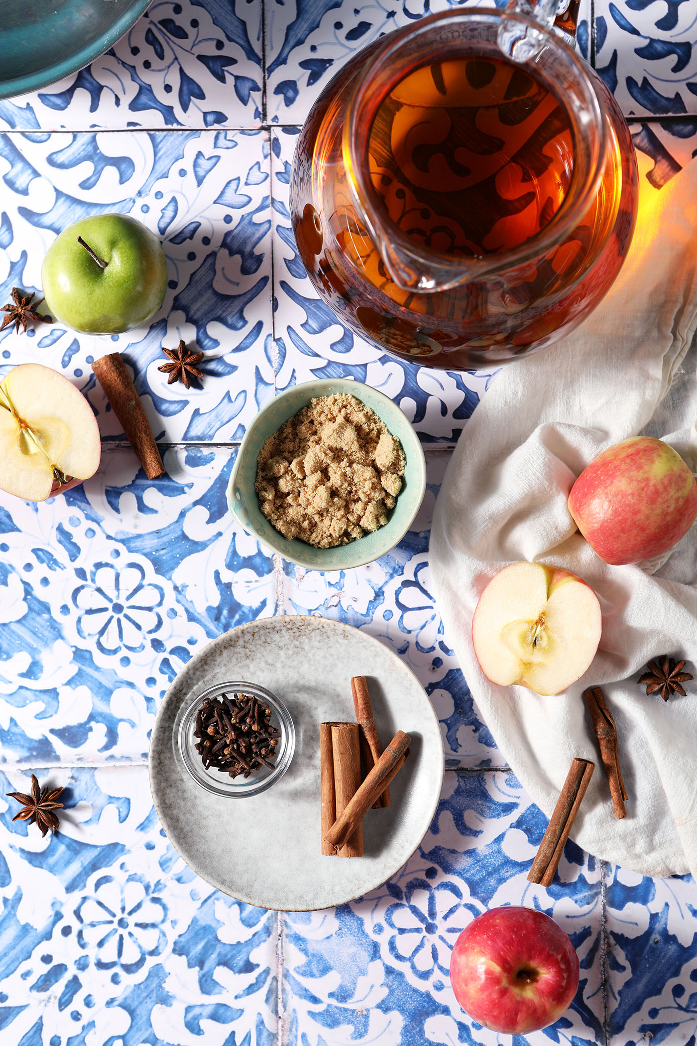 Ingredients to make easy spiced apple cider in bowls, and plates on a blue patterned tile surface