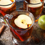 Close up of three glasses of hot Spiced Apple Cider topped with apple slices on a silver platter