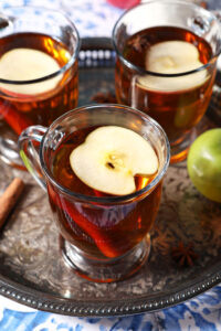 Close up of three glasses of hot Spiced Apple Cider topped with apple slices on a silver platter
