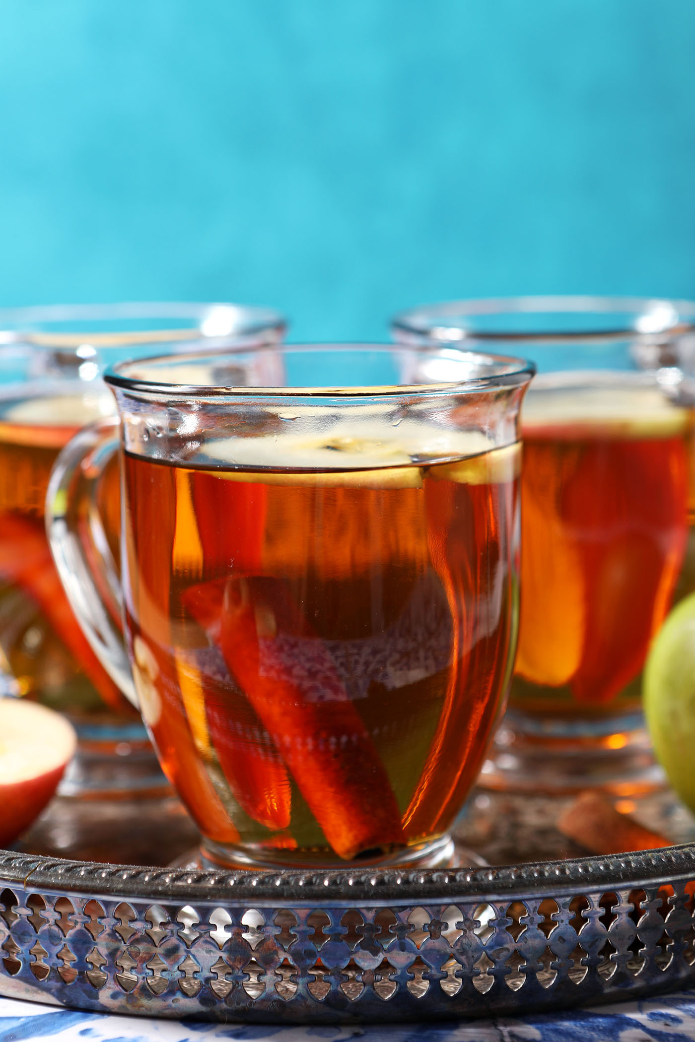 Side angle of three cups of homemade easy spiced cider in mugs on a silver platter in front of a blue wall