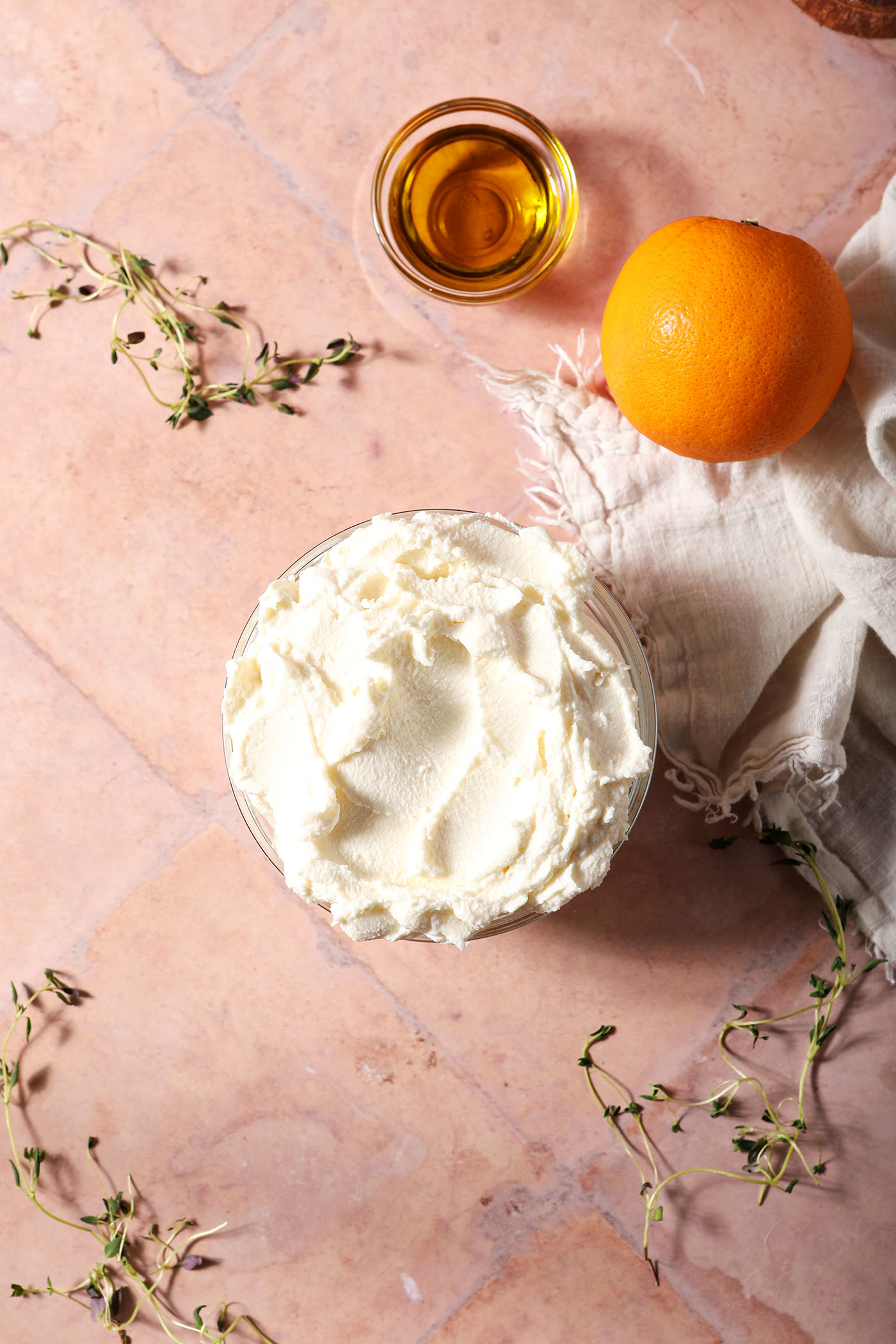 Ingredients to make whipped ricotta on a terracotta surface surrounded by fresh thyme sprigs