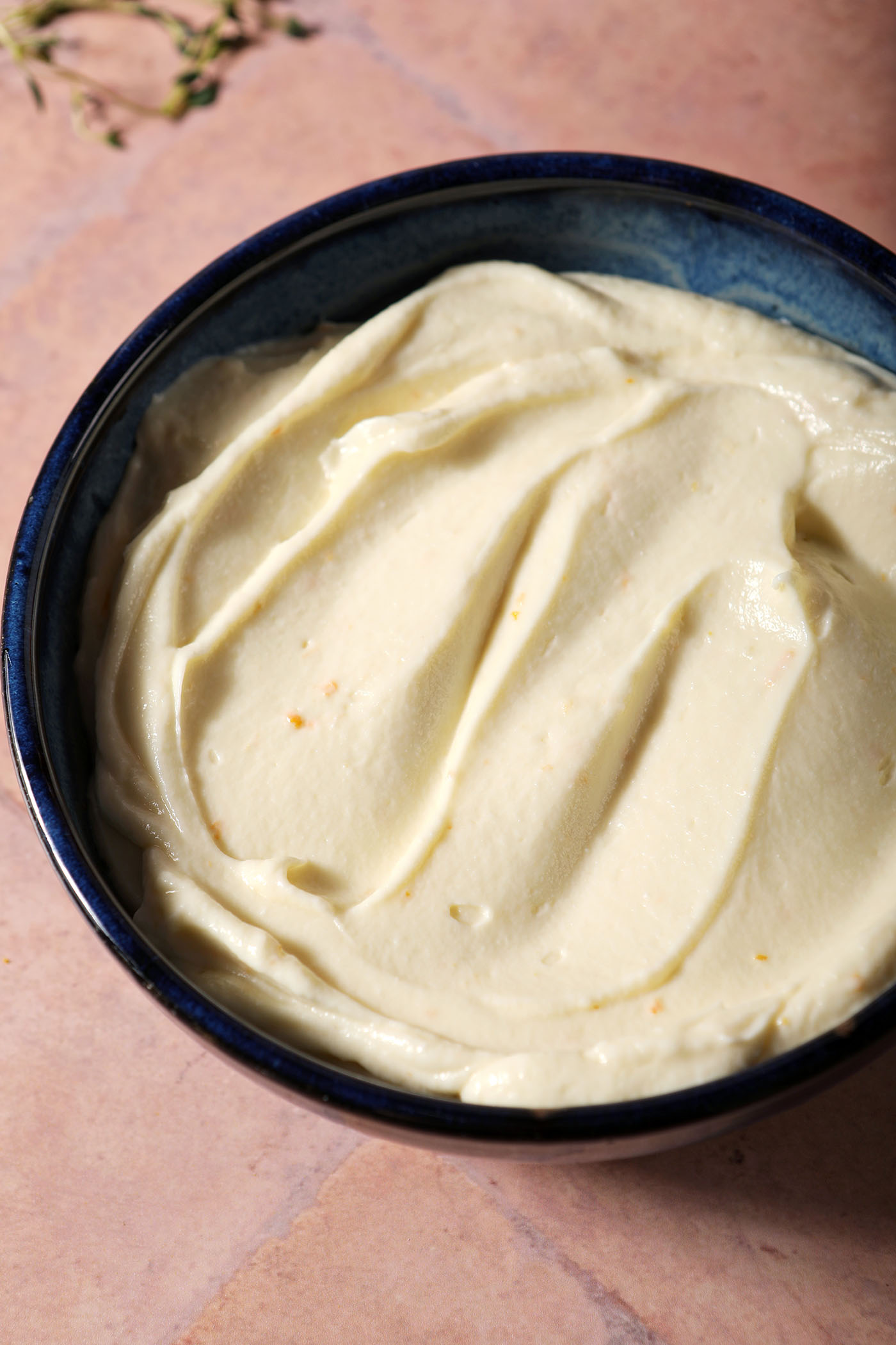 A bowl holds creamy whipped ricotta on a terracotta tiled surface