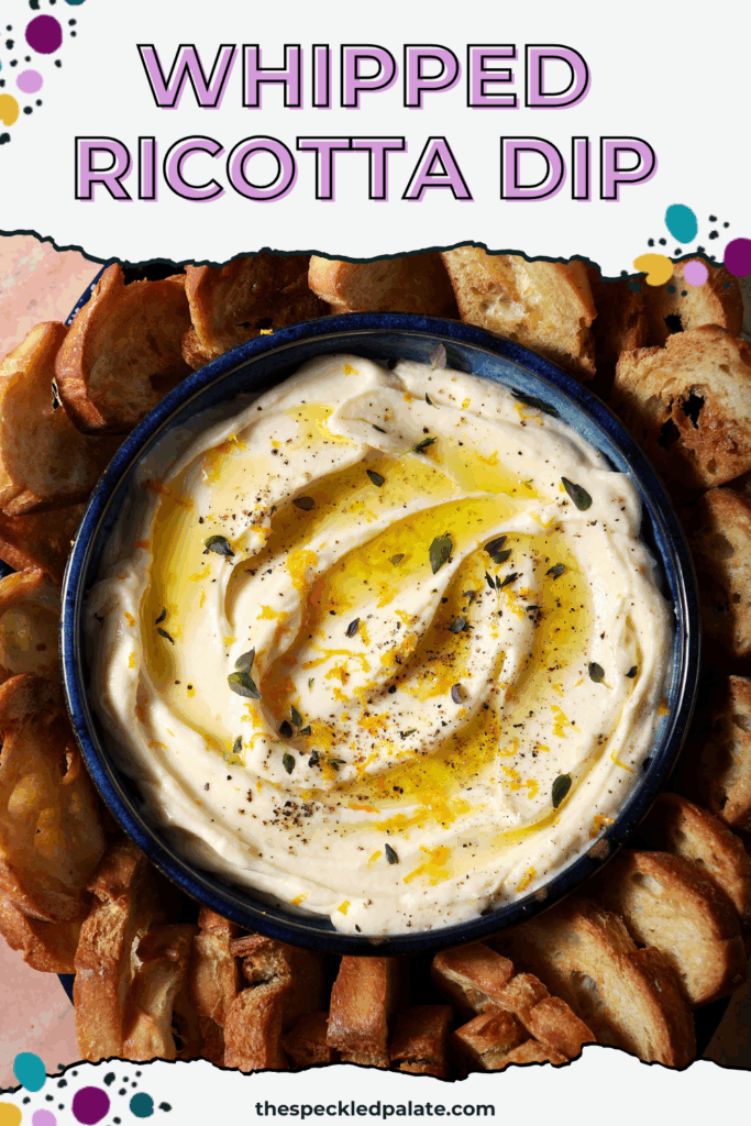 A bowl of whipped ricotta dip garnished with extra thyme, orange zest and olive oil surrounded by crostini on a terracotta surface with the text whipped ricotta dip
