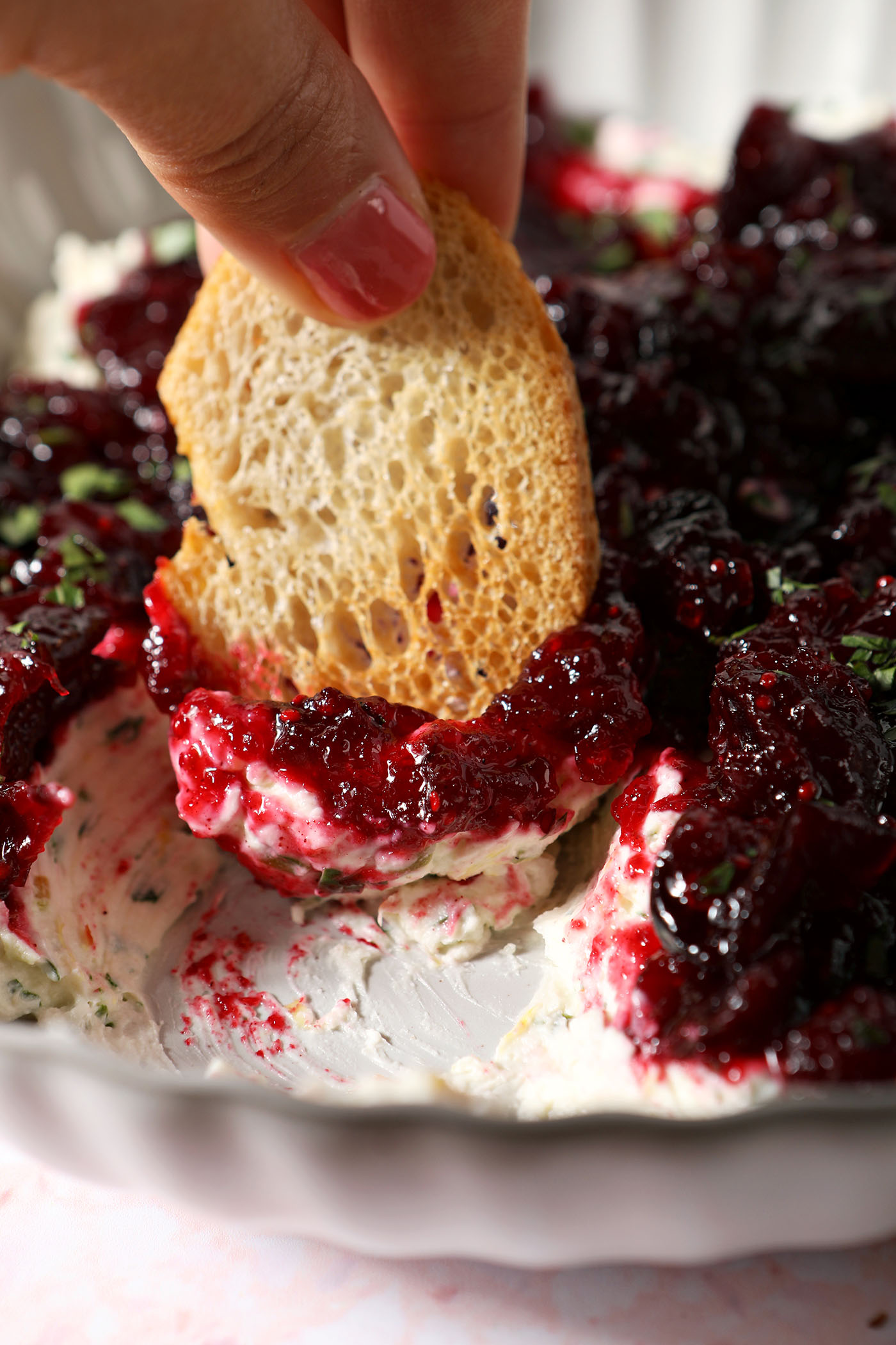 A piece of bread dips into a bowl of creamy cranberry dip